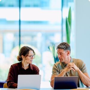 Two people talking, each with a laptop